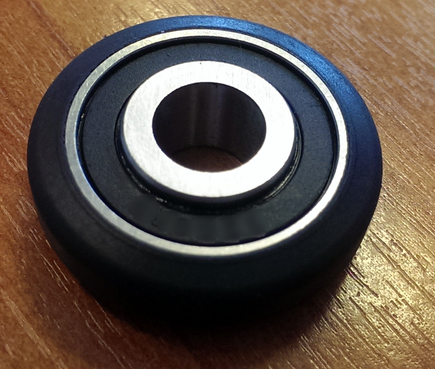 Black plastic roller wheel with an integrated sealed ball bearing, photographed on a wood surface
